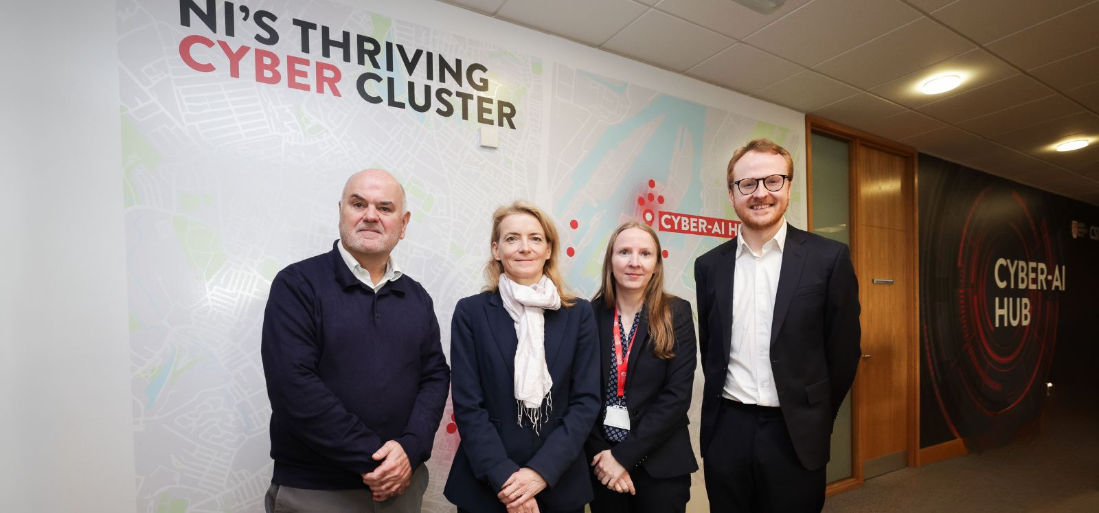 A group of people (Paul Miller, Minister Lloyd, Máire O'Neill, Sam Donaldson) standing in front of a hot map of the NI Cyber Security ecosystem